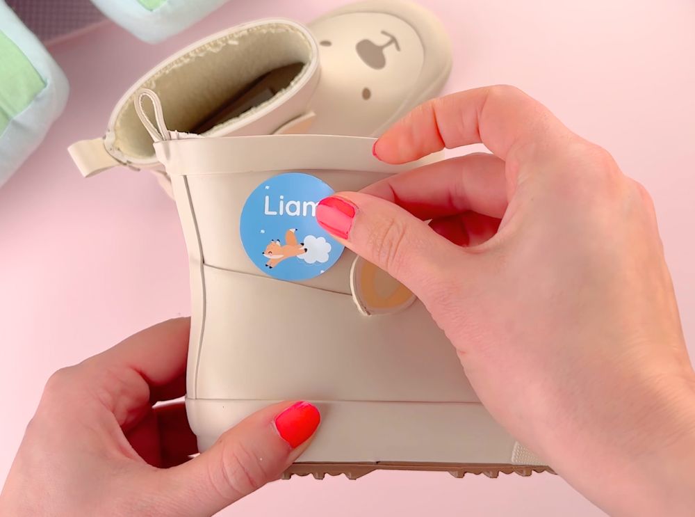 Guide: olika typer av namnlappar – så väljer du rätt 3 Rund blå namnlapp med rävmotiv fästs på en beige barnstövel