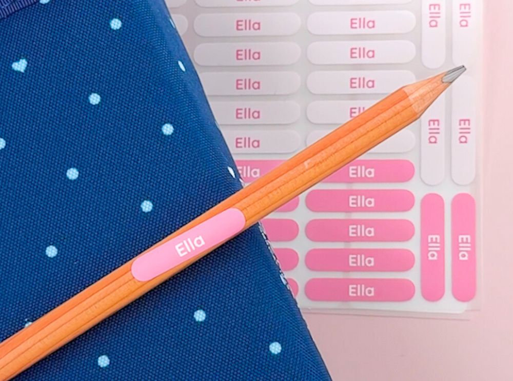 Guide: olika typer av namnlappar – så väljer du rätt 4 Rosa namnlapp med namnet ella på en penna, bredvid ett matchande klistermärkesark