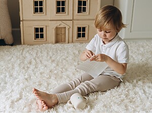 Litet barn som sitter på en mjuk matta och drar av en namnlapp från ett klistermärkesark i ett mysigt lekrum