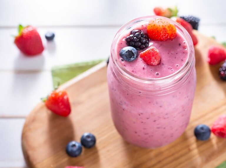 Närbild av en rosa uppfriskande smoothie toppad med färska bär
