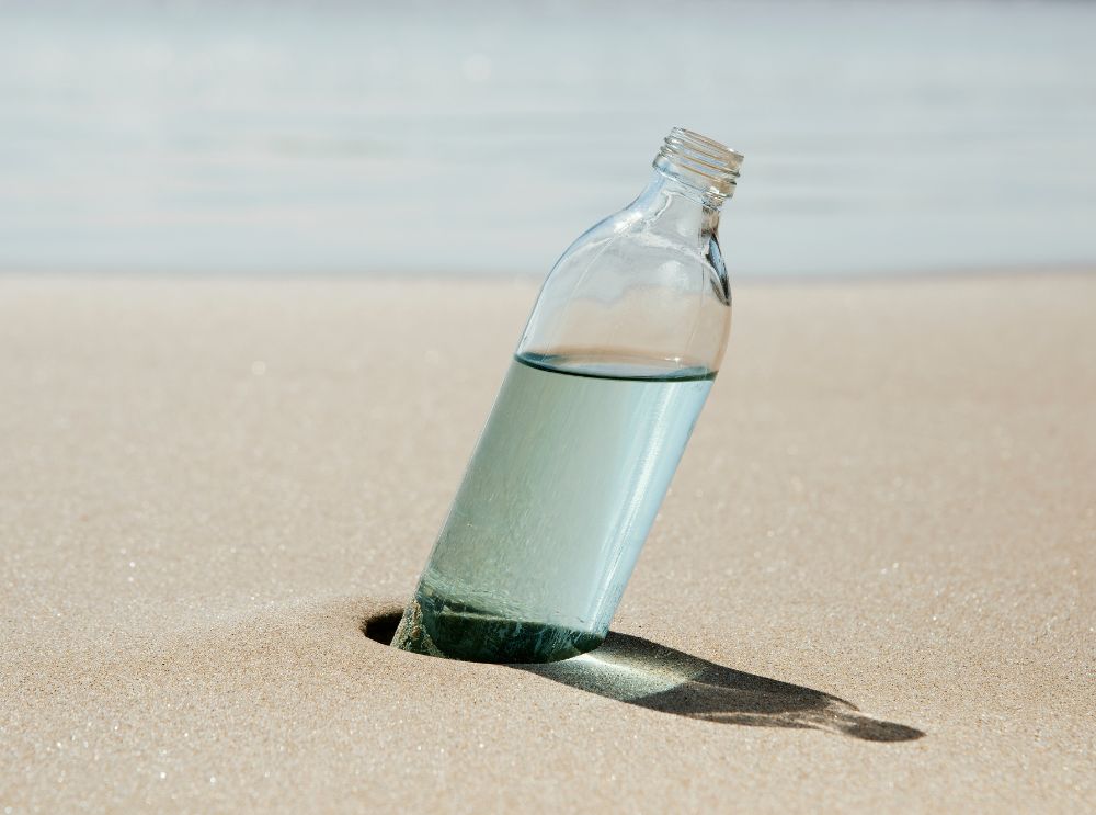 Vattenflaska stående i sanden på en strand.