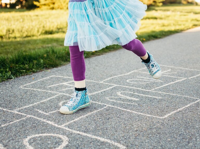 Barn som hoppar hage på trottoaren, klädd i färgglada sneakers