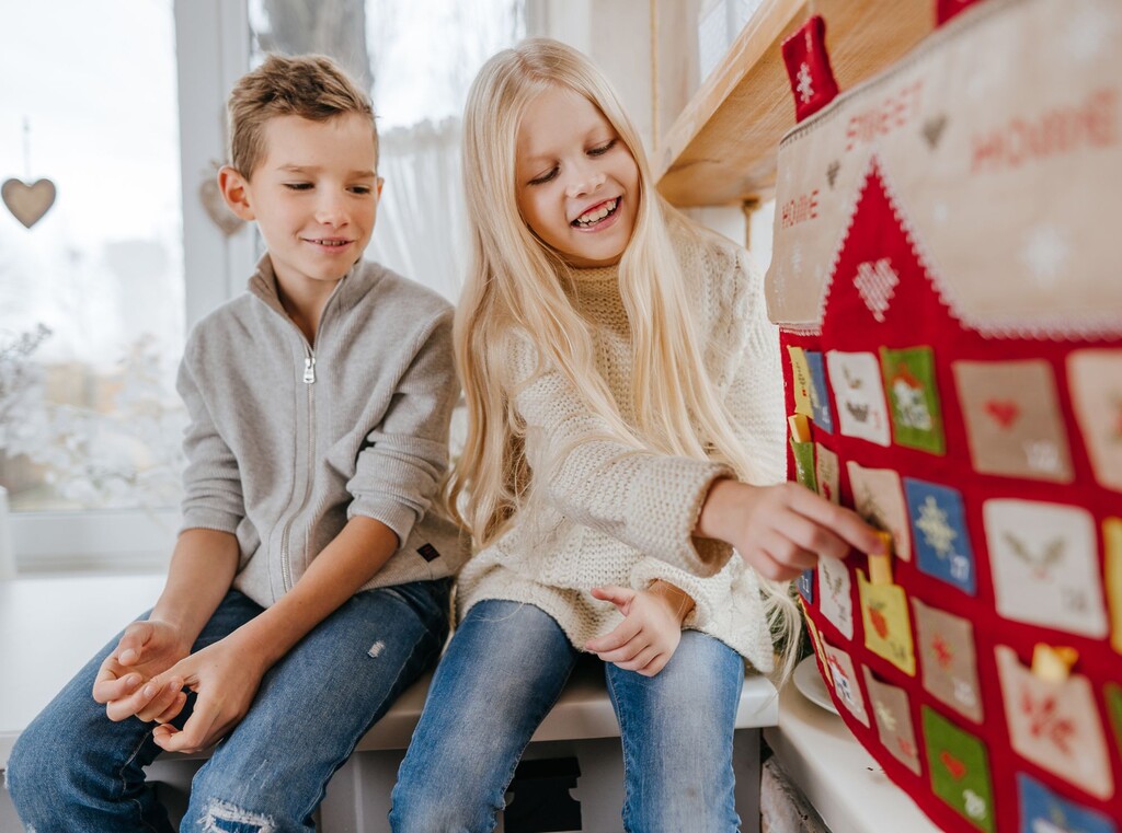 Två barn som sitter tillsammans och öppnar små luckor på en julig adventskalender