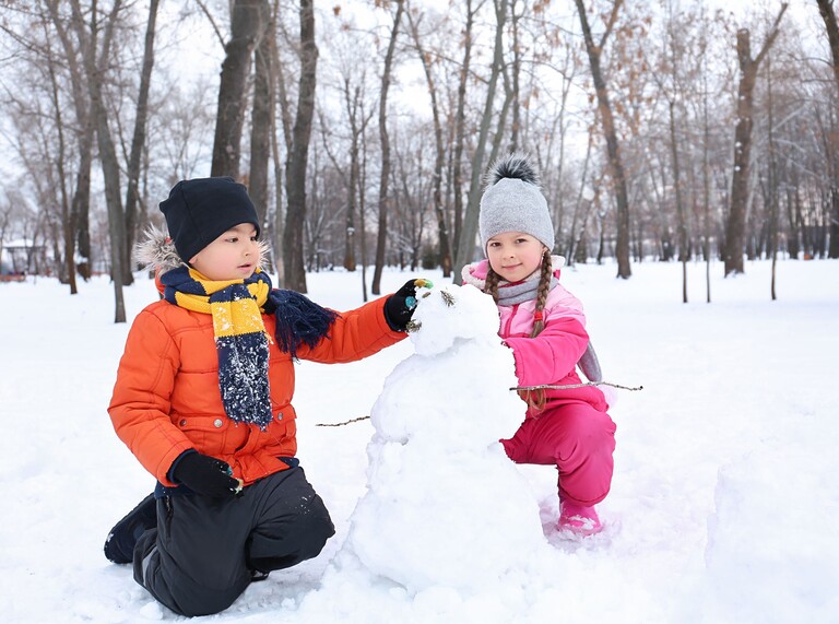 Två barn som leker i snön och bygger en snögubbe tillsammans i en vinterpark
