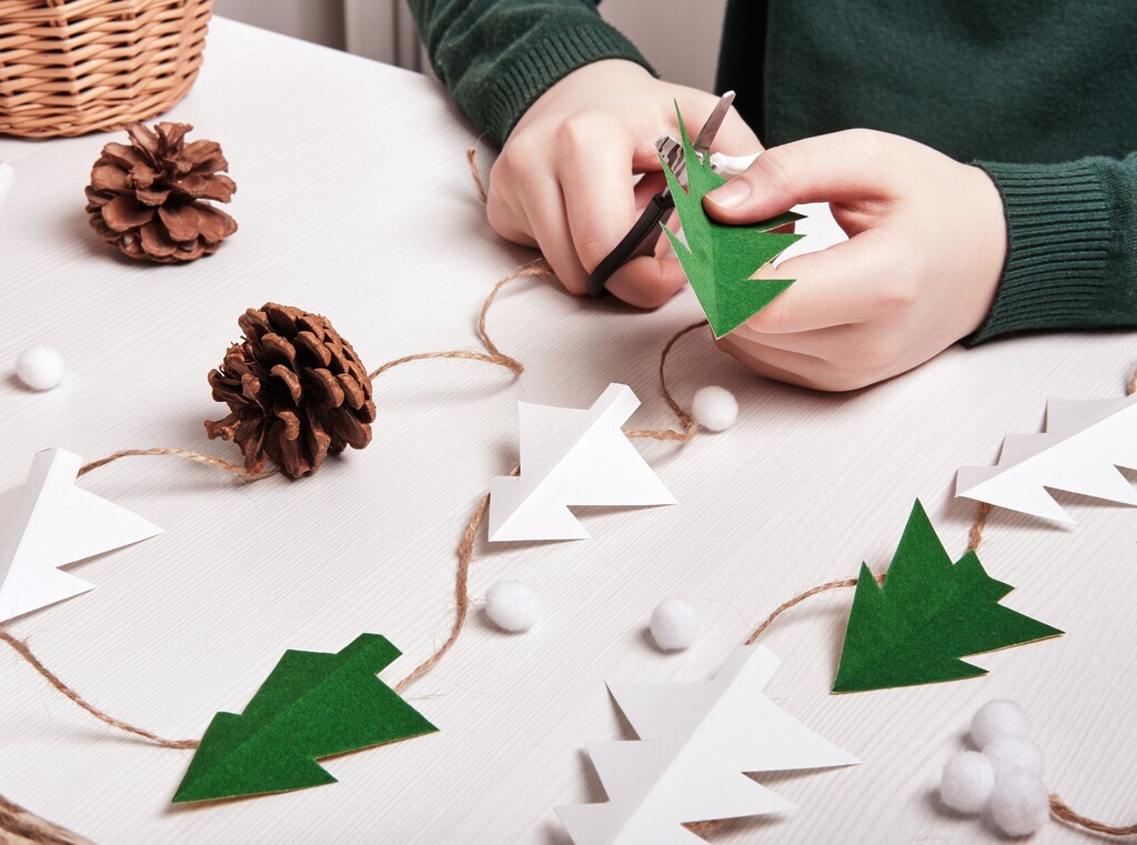 Julpyssel med barn: enkla dekorationer att göra hemma 5 Barn som pysslar en julgirlang med pappersgranar, kottar och snöre som ett mysigt julpyssel.