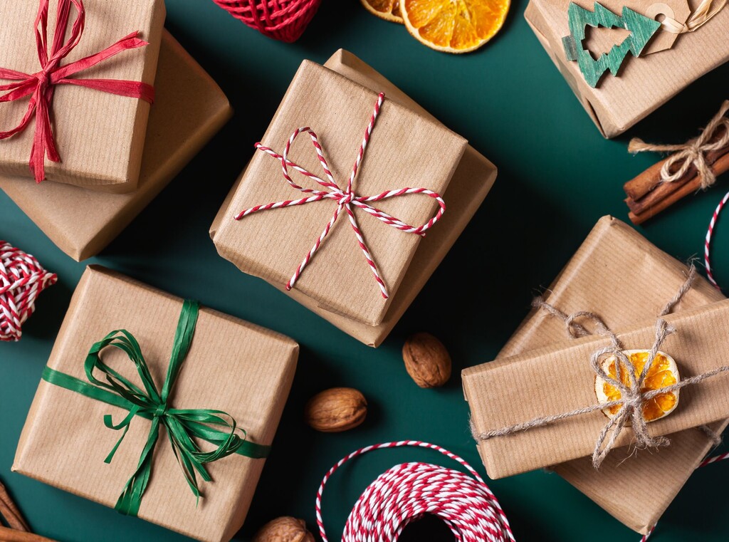 Flatlay med julklappar i brunt presentpapper på mörkgrön bakgrund med torkad apelsin och kanel.