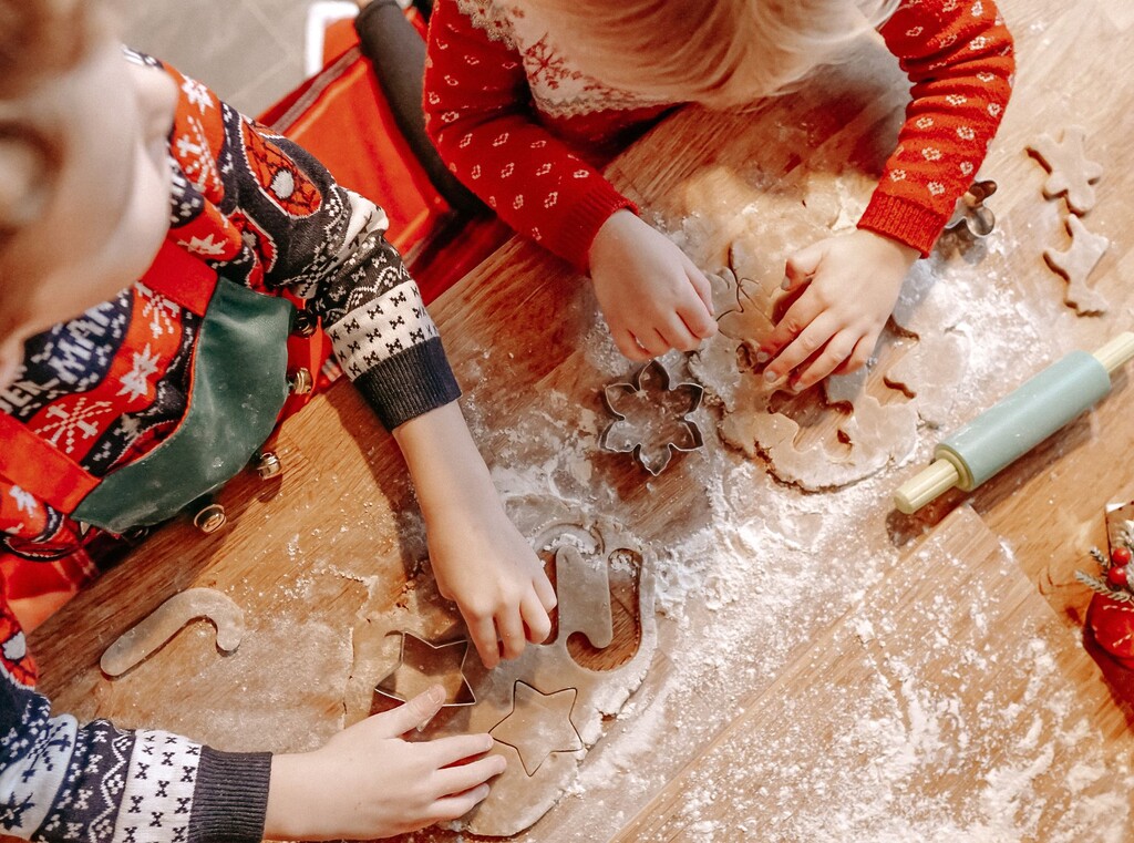 Barnhänder som stansar ut pepparkaksdeg med kakformar, sedda uppifrån.