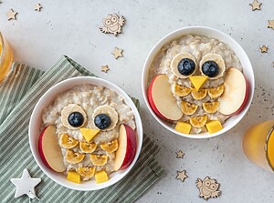 Söta uggleformade havregrynsskålar dekorerade med frukt för en barnvänlig frukost