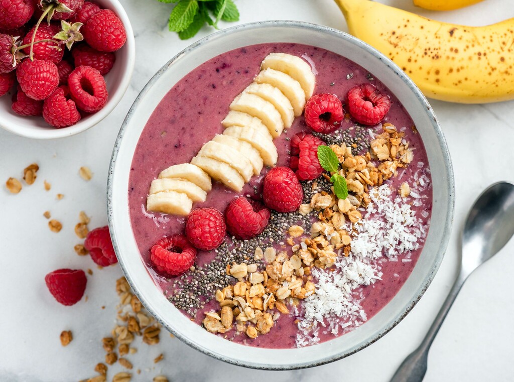 Bärsmoothiebowl toppad med bananskivor, hallon, granola och chiafrön.