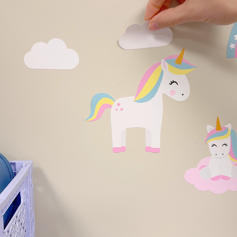Wallstickers med enhörning, regnbågar och blommor som placeras på vägg