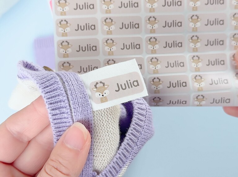 Personaliserad namnlapp med hjortmotiv och namnet Julia fäst på lila stickad tröja