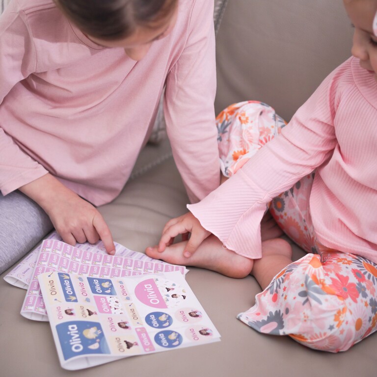 Två barn i rosa pyjamas tittar på ark med stora namnlappar med Olivia-motiv