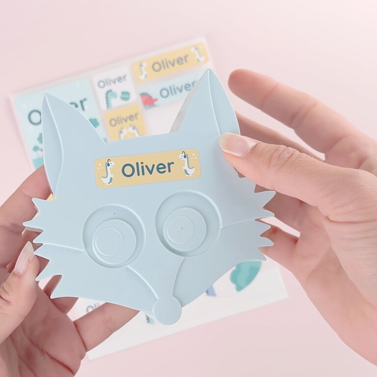 Ljusblå räv-formad mask märkt med stor Oliver-namnlapp och ark med fler namnlappar