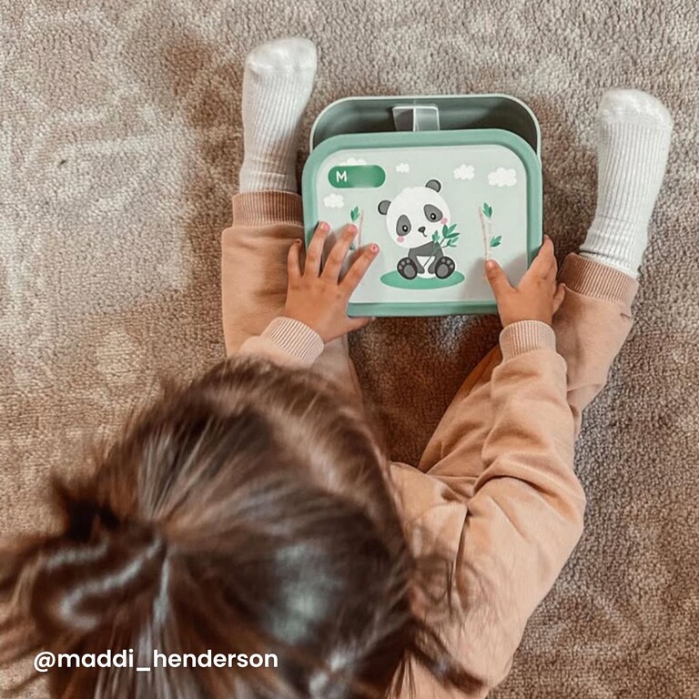 Litet barn håller grön matlåda med pandadesign och namnet M
